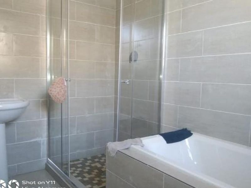 A modern bathroom featuring a pedestal basin, a glass-enclosed shower, and a built-in bathtub with neutral wall tiling throughout.