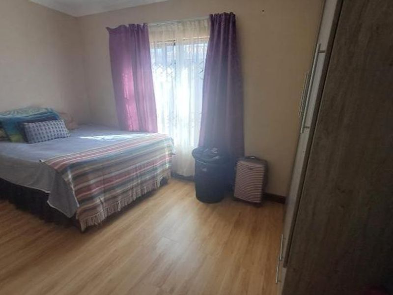 A functional bedroom featuring laminate flooring, a built-in wardrobe, and a window fitted with a security gate.