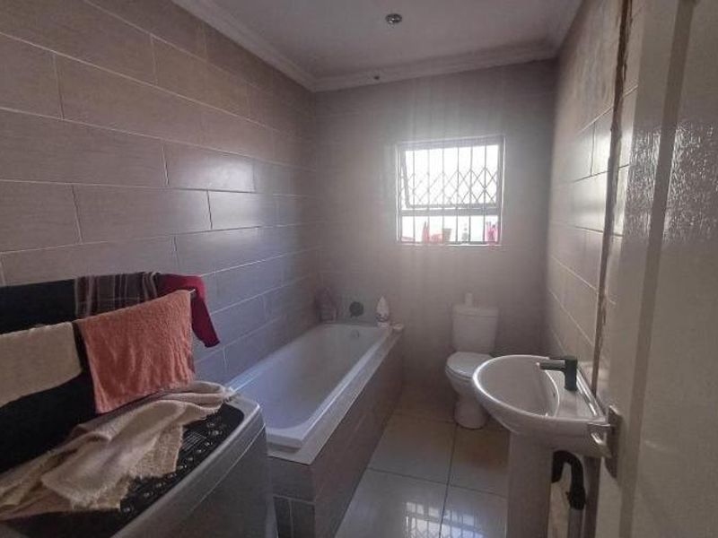 A functional bathroom featuring a built-in bathtub, pedestal basin, toilet, and full-height wall tiling with a window providing natural light.