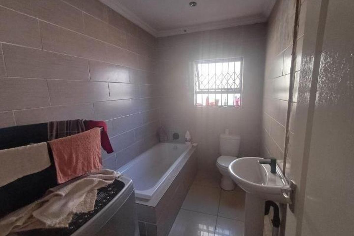A functional bathroom featuring a built-in bathtub, pedestal basin, toilet, and full-height wall tiling with a window providing natural light.
