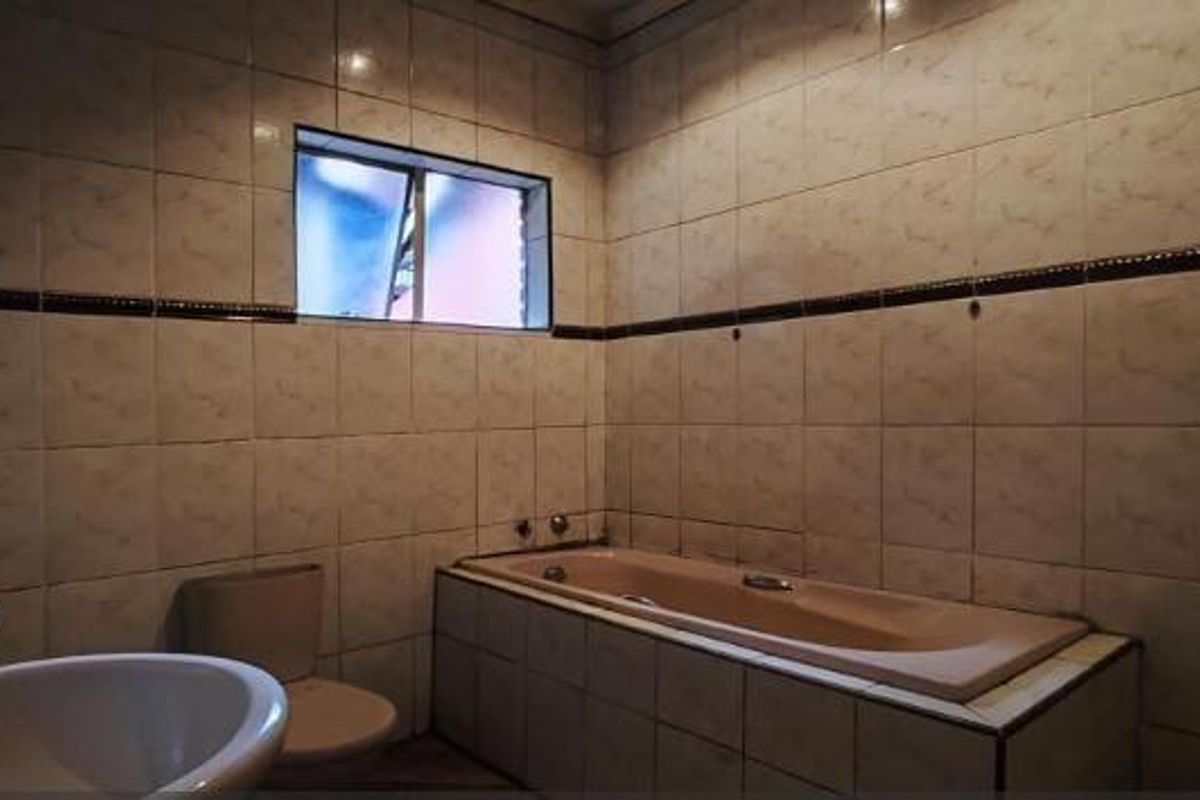 A dated bathroom featuring a built-in bathtub, pedestal basin, and full-height ceramic wall tiling.