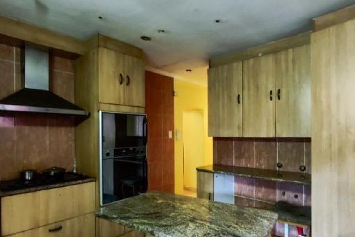 A functional kitchen featuring wood-tone cabinetry, granite countertops, a built-in oven, and a stainless steel extractor fan with tiled splashbacks.