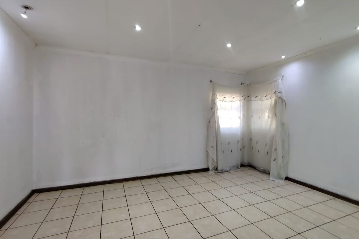 An empty bedroom featuring neutral ceramic floor tiles, recessed downlighting, and plain white walls, offering a blank canvas for interior design.