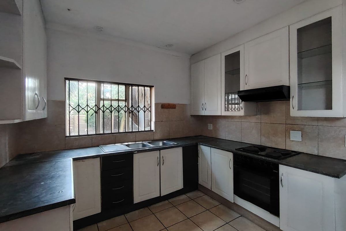 A functional kitchen featuring white cabinetry, dark countertops, built-in oven and hob, tiled flooring, and a window with security bars.