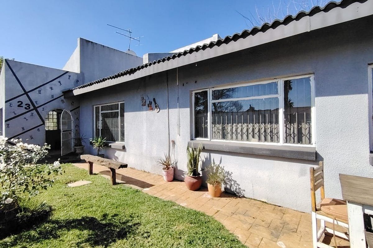 Rear exterior view of the house featuring a paved walkway, security gates, and windows with security bars.