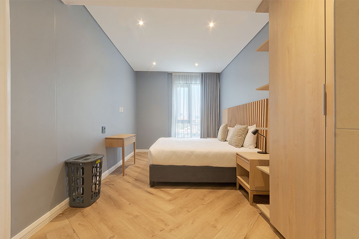 Modern bedroom featuring herringbone wood flooring, recessed lighting, and custom built-in timber headboard and shelving units with access to a private balcony.