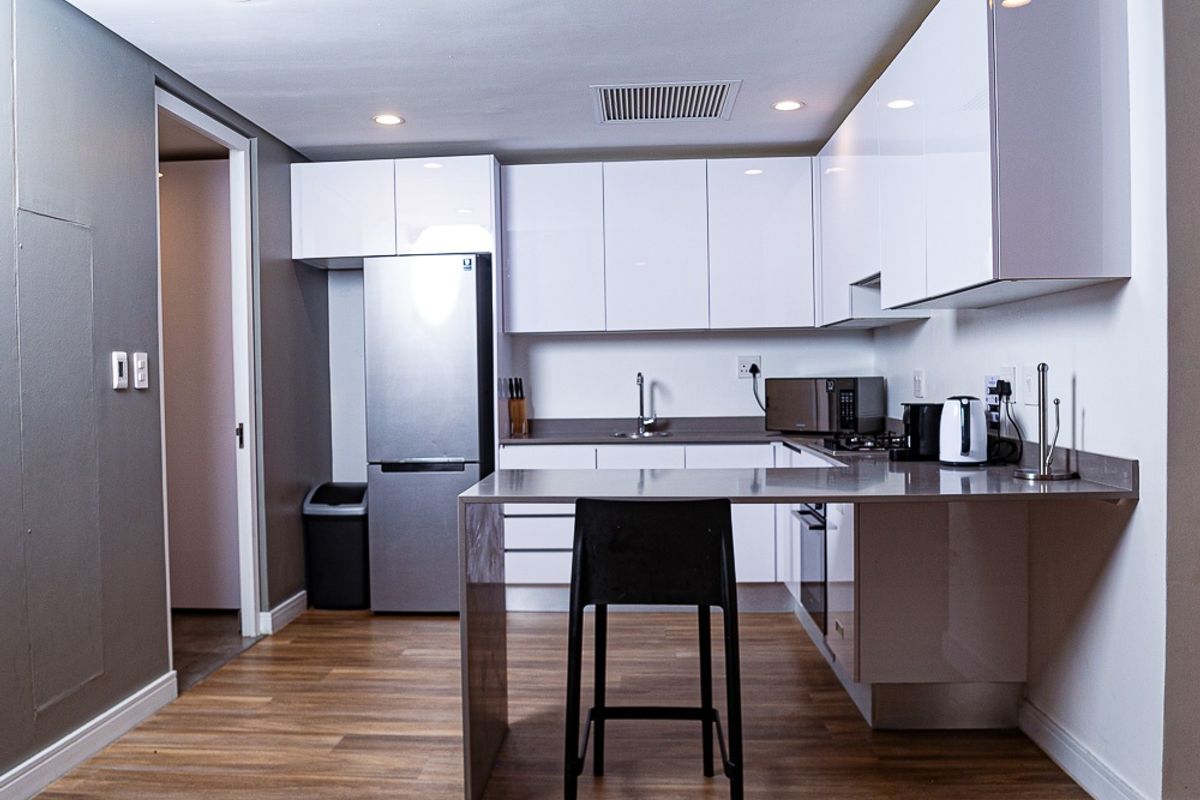 Modern kitchen featuring sleek white cabinetry, stone countertops, integrated appliances, and a breakfast bar, finished with durable laminate flooring and recessed lighting.