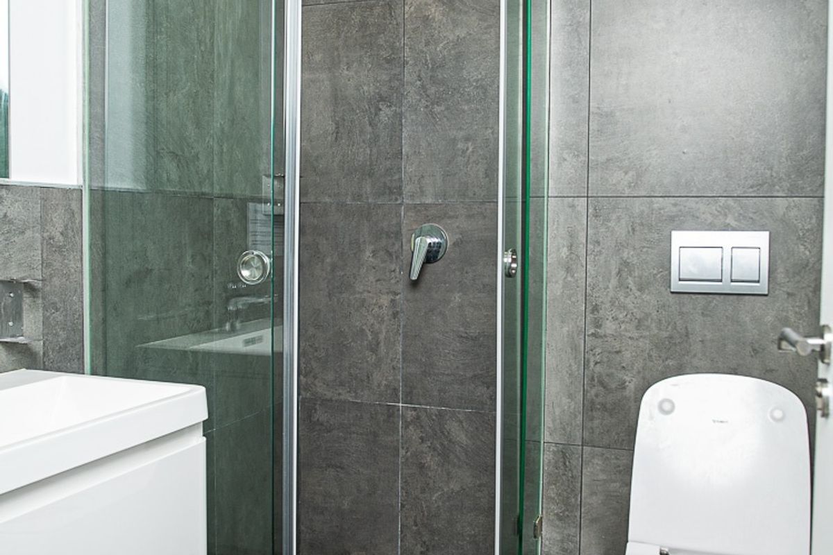 Modern bathroom featuring a walk-in shower with glass enclosure, wall-mounted toilet, and contemporary large-format grey tiling throughout.