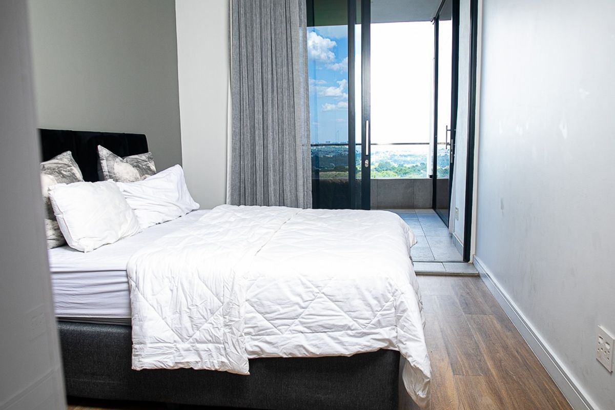 A modern bedroom featuring laminate flooring and a large sliding glass door providing direct access to a private balcony with scenic views.
