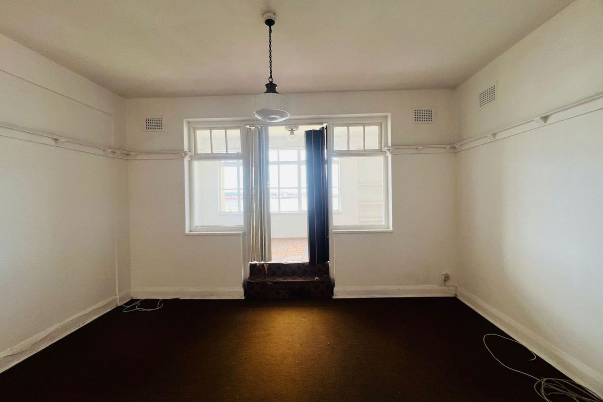 An empty living room featuring original picture rails, a central pendant light, and direct access to an outdoor balcony area.