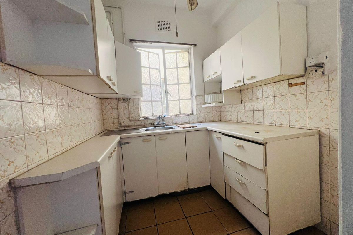 A compact, dated kitchen featuring white cabinetry, tiled splashbacks, and a single basin sink, offering potential for a modern renovation.