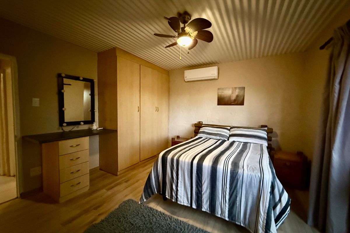A bedroom featuring built-in cupboards, a ceiling fan, and a wall-mounted air conditioning unit, finished with laminate flooring and a textured ceiling.