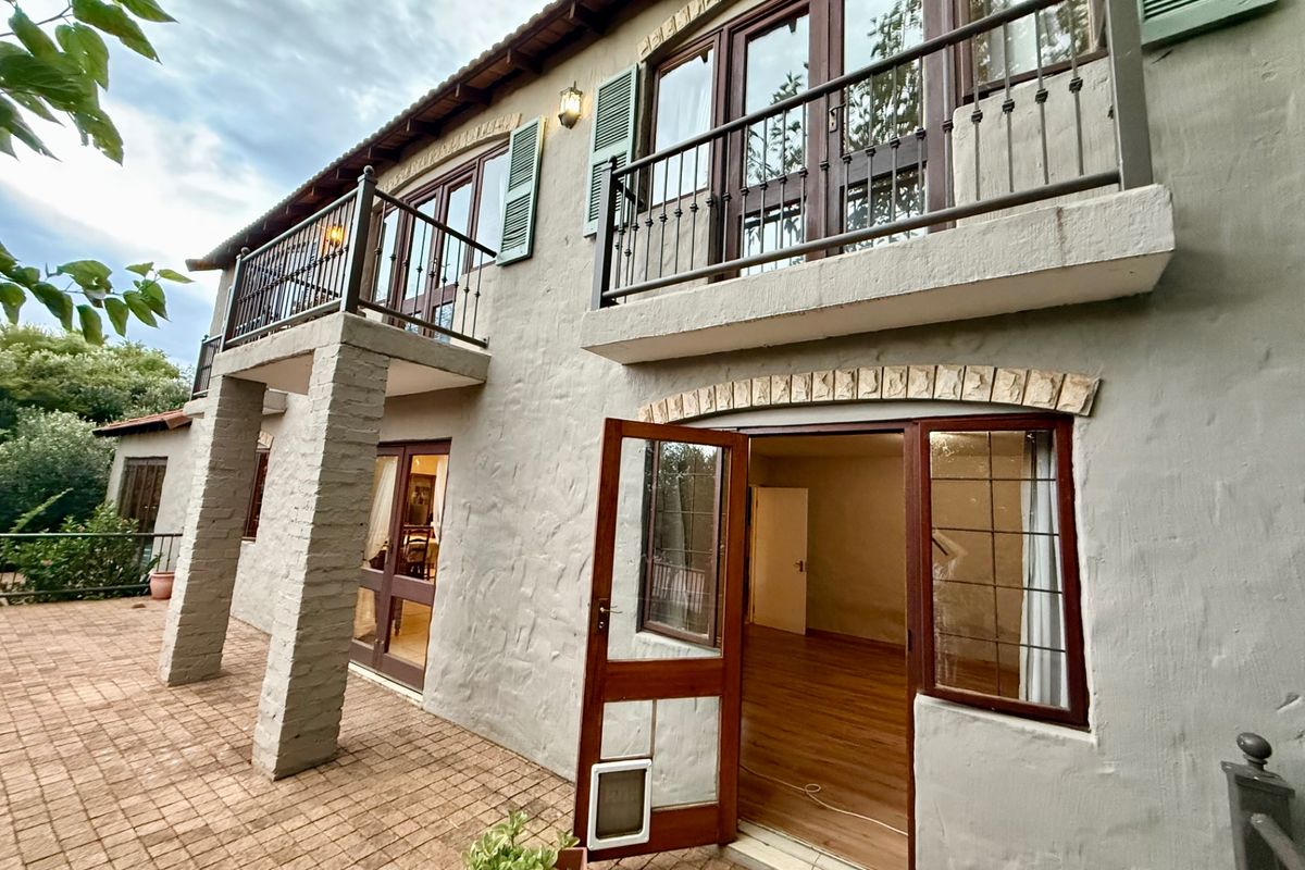 Rear elevation of a two-story residence featuring a brick-paved patio, upper-level balconies with wrought iron railings, and timber-framed doors and windows.