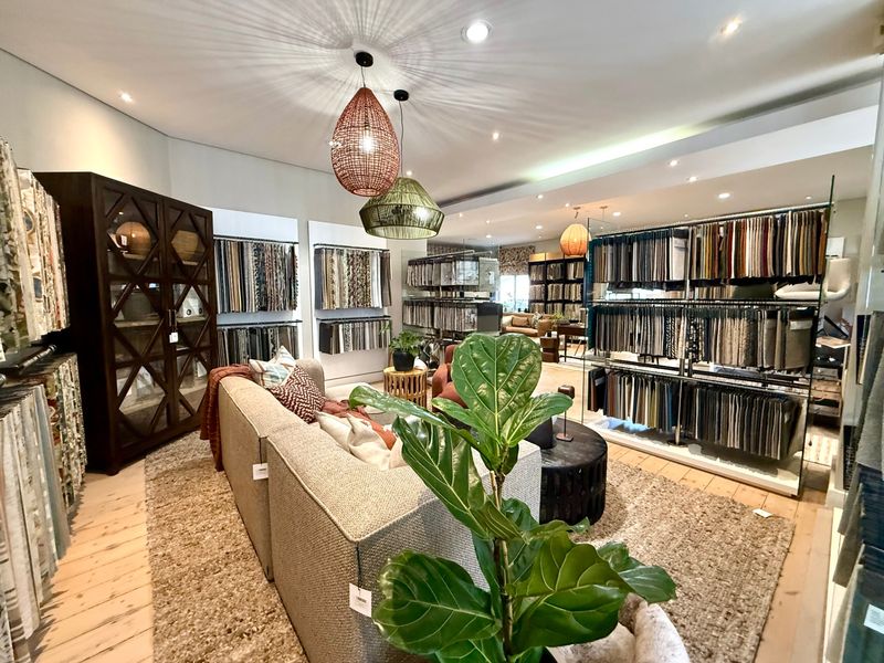 A well-lit commercial showroom space featuring timber flooring, recessed ceiling lights, and extensive built-in display shelving for fabric samples.