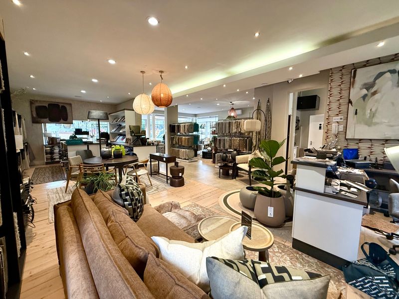 A well-lit, open-plan commercial showroom space featuring timber flooring, recessed downlighting, and cove lighting, currently utilized for interior design and furniture display.