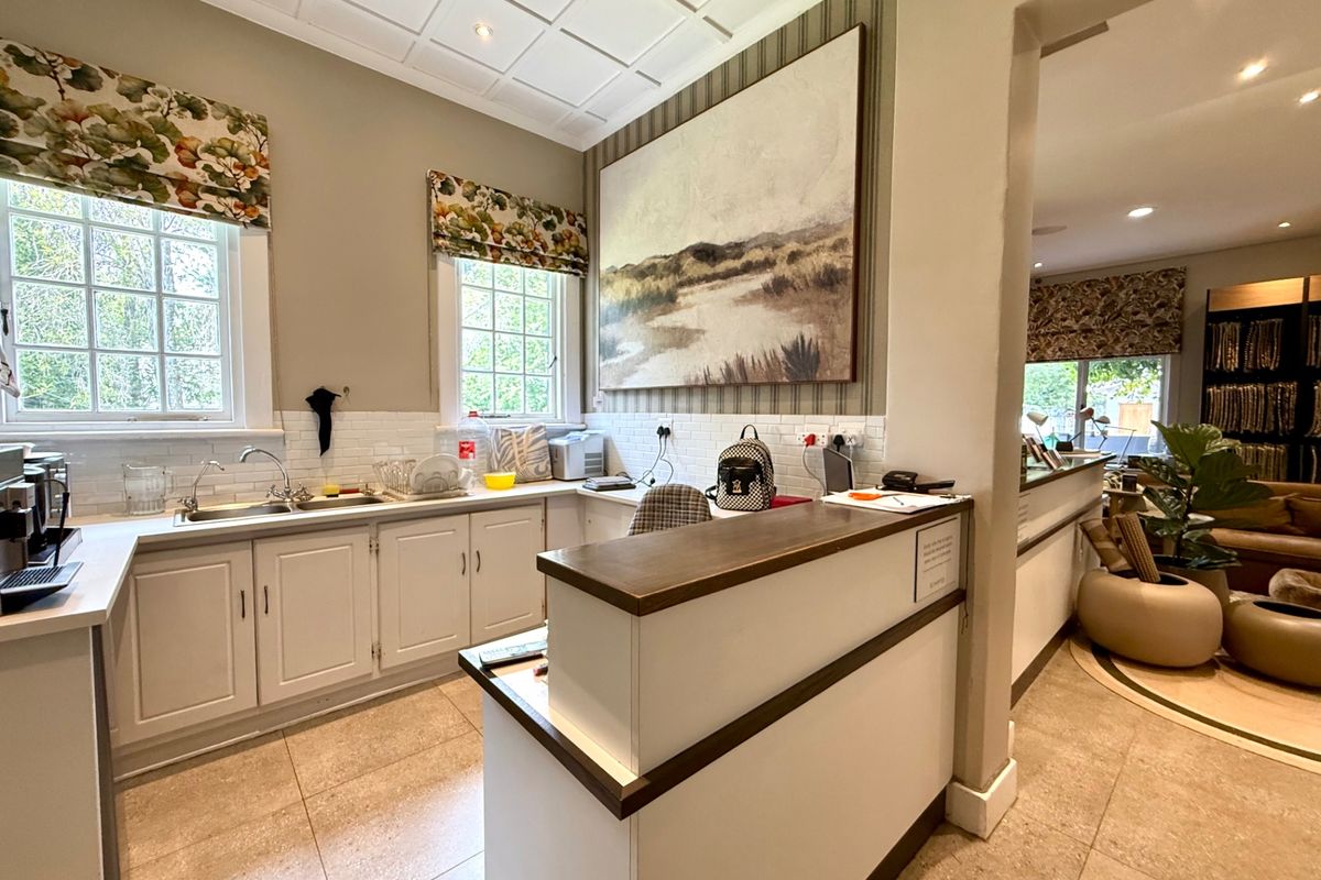 A well-maintained kitchen area featuring white cabinetry, tiled backsplash, double sink, and a coffered ceiling, with an adjacent open-plan living space.