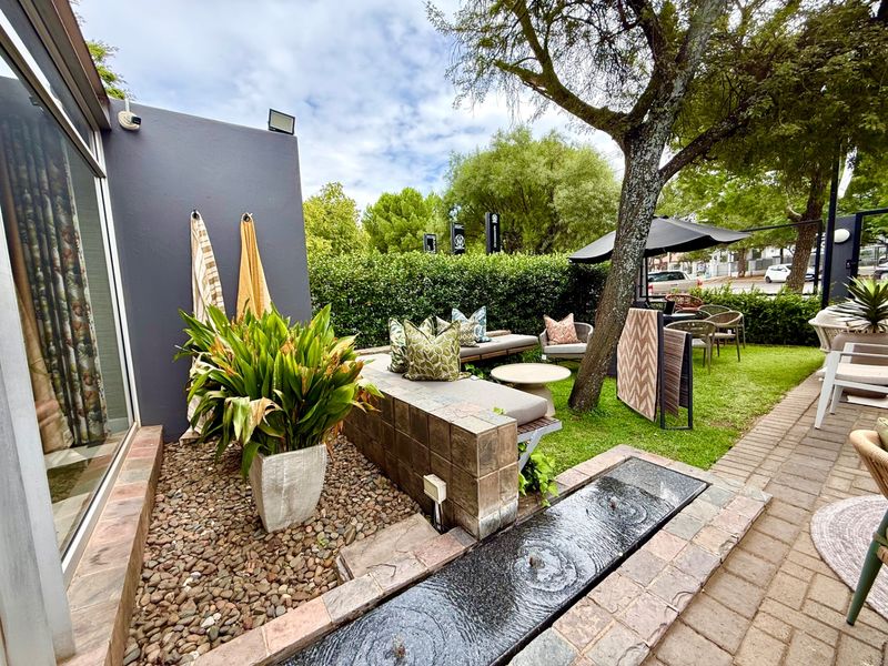 A landscaped outdoor patio area featuring a built-in stone bench, a decorative water feature, and paved flooring, set within a private garden space.