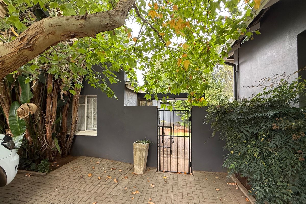 A private rear courtyard area featuring paved flooring, a secure metal gate, and mature trees providing shade against the dark-painted exterior walls.