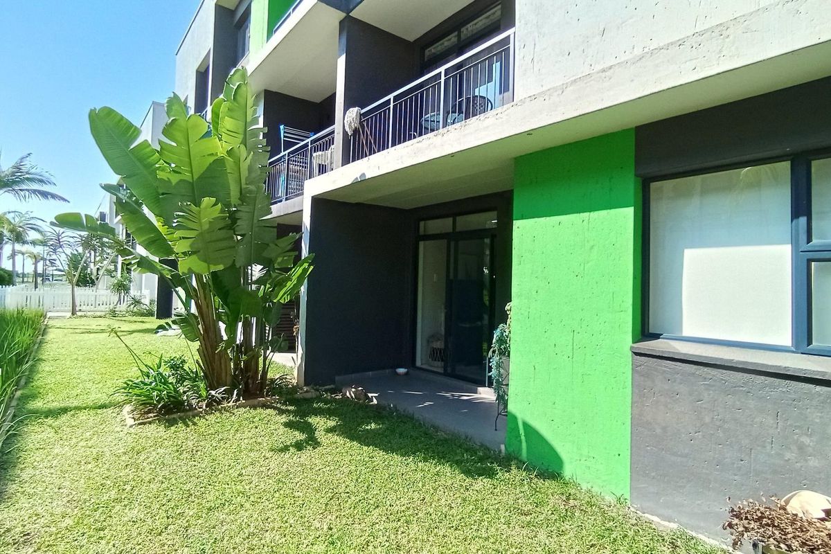 Rear view of the apartment building featuring a ground floor patio, upper level balcony with metal railings, and a well-maintained private garden area.