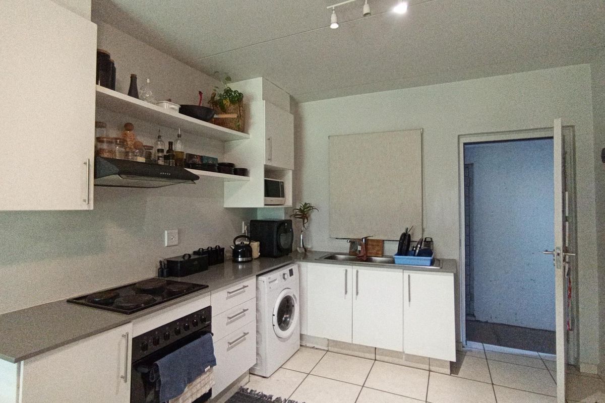 A functional kitchen featuring white cabinetry, a built-in stove and oven, stainless steel sink, and tiled flooring with space for a washing machine.