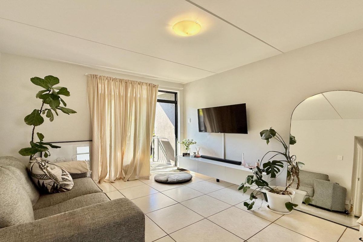 A bright living room featuring large floor tiles, a wall-mounted media console, and a sliding glass door providing access to an outdoor area.