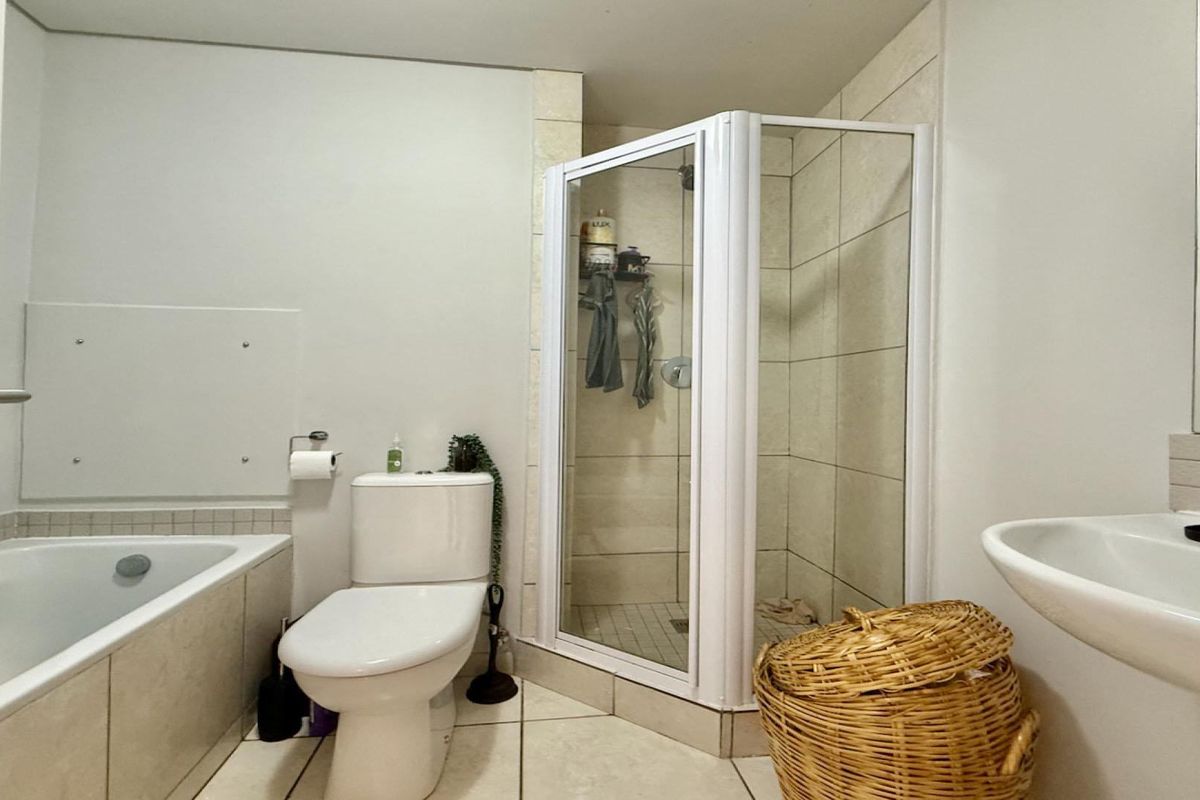 A functional bathroom featuring a built-in bathtub, a separate corner shower enclosure, a wall-mounted basin, and neutral ceramic tiling throughout.