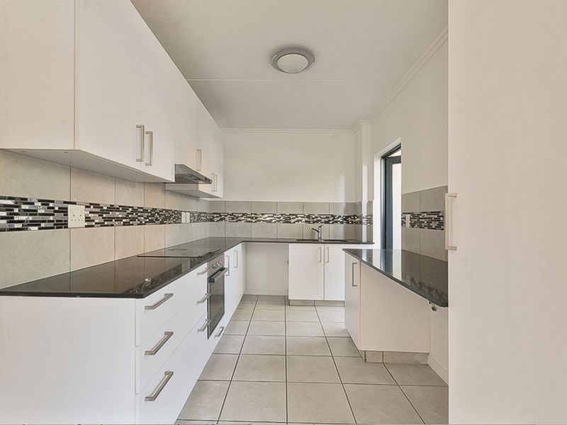 A clean, modern kitchen featuring white cabinetry, dark granite countertops, a built-in oven, and a decorative tiled backsplash.