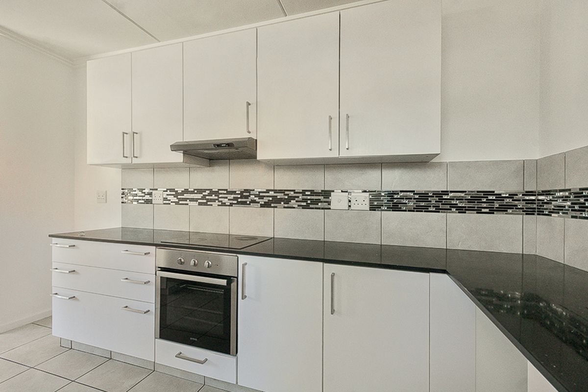 A clean, modern kitchen featuring white cabinetry, black granite countertops, integrated oven and hob, and a decorative tiled backsplash.