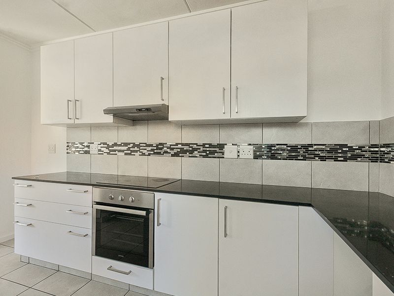 A clean, modern kitchen featuring white cabinetry, black granite countertops, integrated oven and hob, and a decorative tiled backsplash.