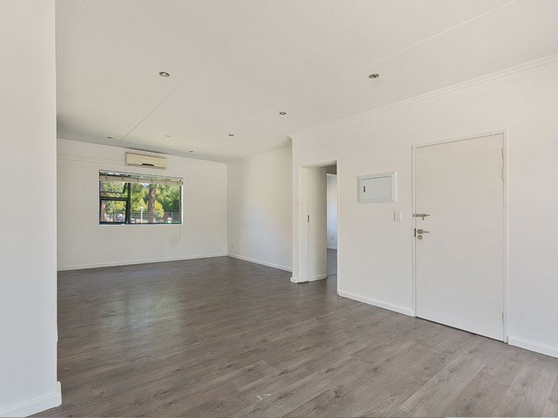 A bright, spacious, and empty living area featuring modern laminate flooring, recessed lighting, and a wall-mounted air conditioning unit.