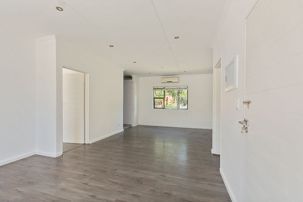 A bright, vacant living area featuring modern laminate flooring, recessed downlighting, and a wall-mounted air conditioning unit.