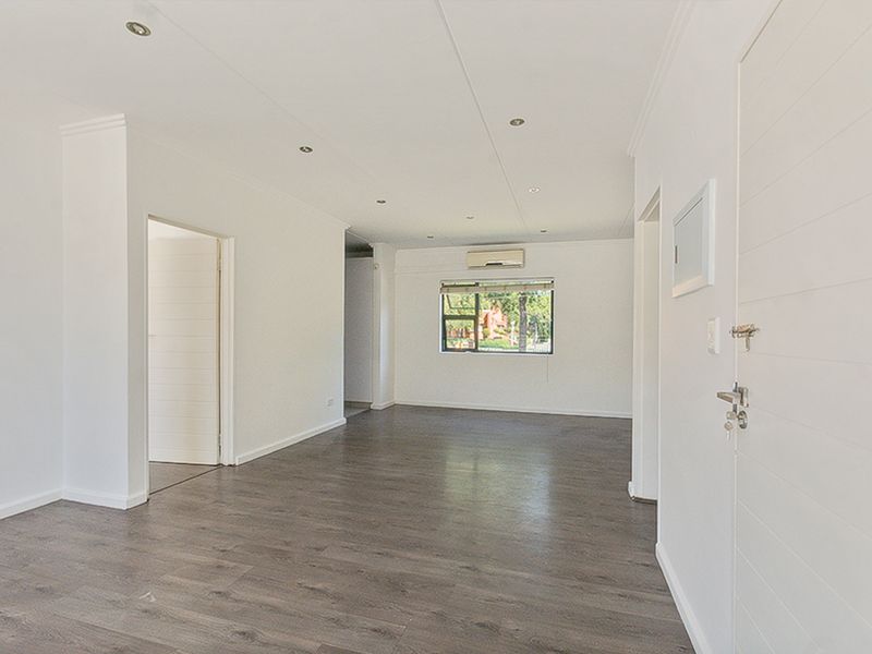 A bright, vacant living area featuring modern laminate flooring, recessed downlighting, and a wall-mounted air conditioning unit.