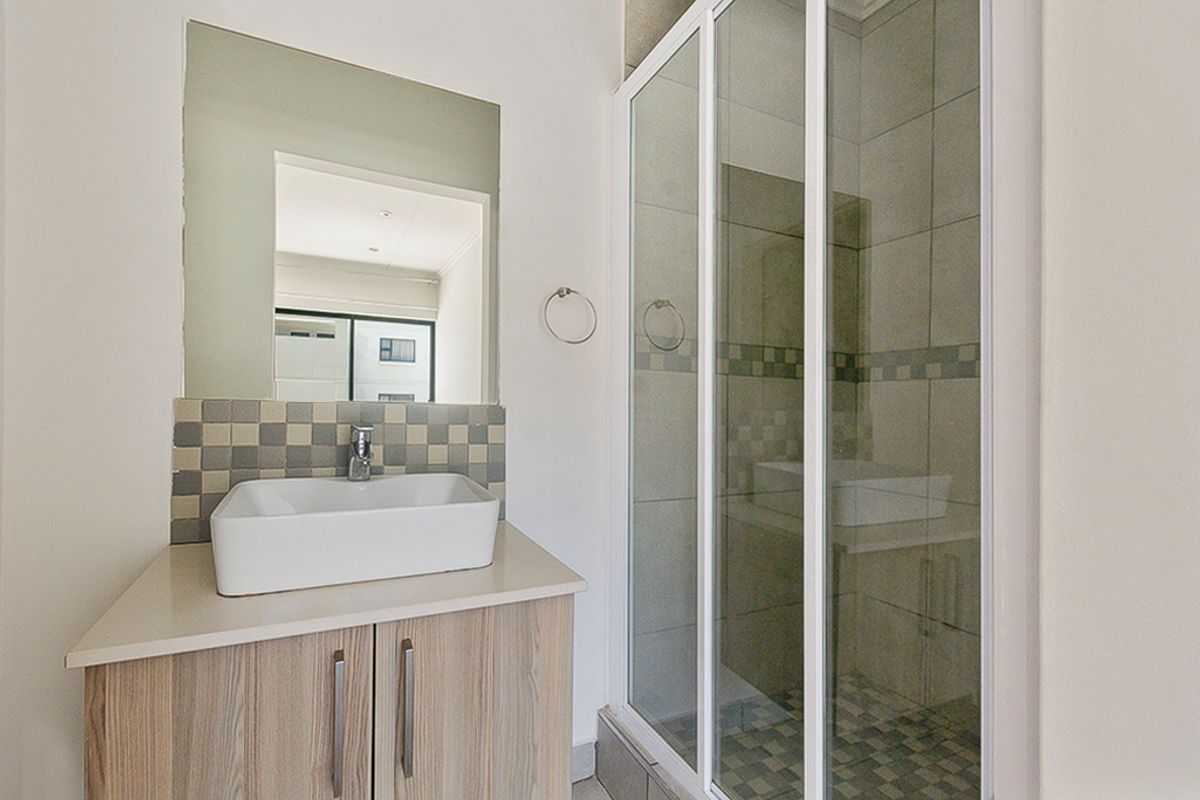 A clean, modern bathroom featuring a vessel sink vanity, tiled splashback, and a glass-enclosed shower with neutral wall tiling.