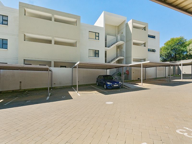 Exterior view of an apartment complex featuring covered parking bays, paved driveway, and external stairwell access.