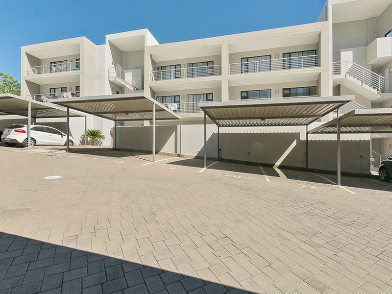 Exterior view of a modern apartment complex featuring covered parking bays and multi-level balconies with metal railings.