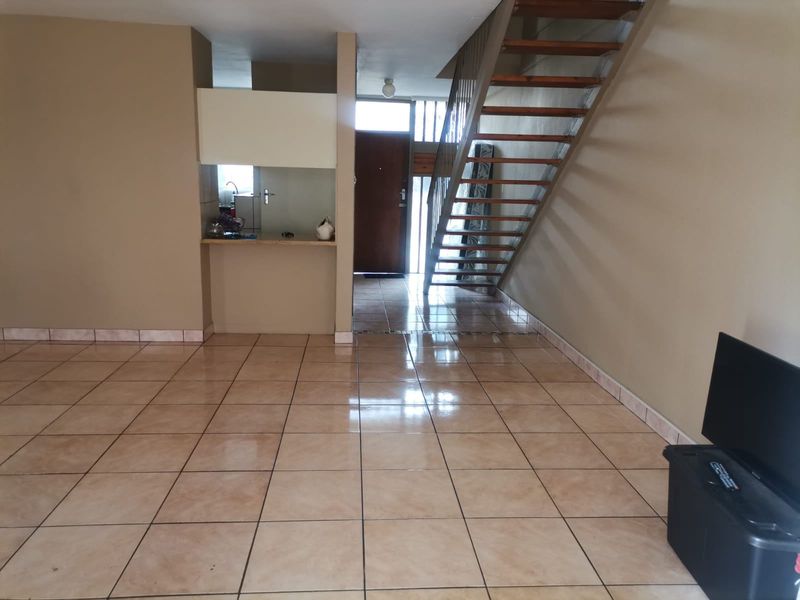 Open plan living area featuring tiled flooring, a staircase, and a compact kitchen nook near the entrance.