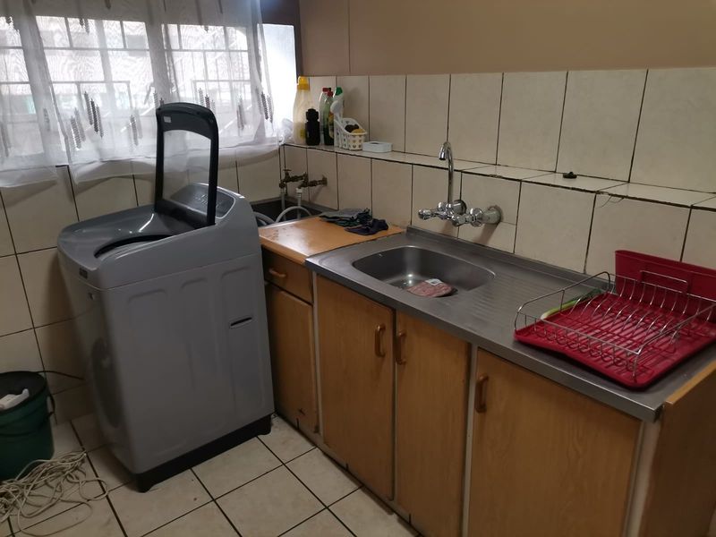 A functional laundry area featuring a stainless steel sink, built-in wooden cabinetry, and tiled walls and flooring.