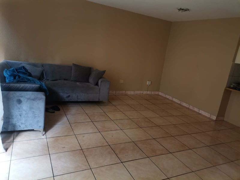 An open plan living area featuring ceramic floor tiles and neutral wall paint, with a partial view of an adjacent kitchen area.