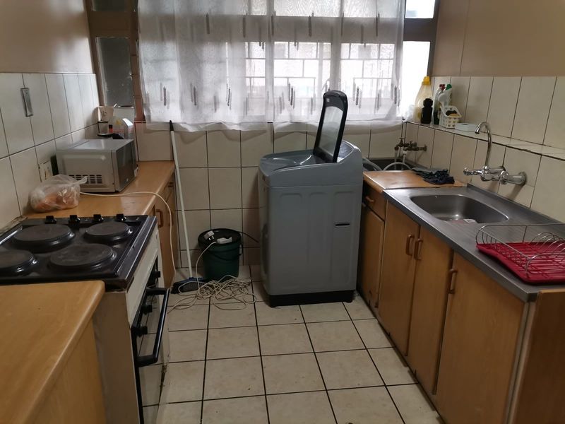 A compact, functional kitchen featuring built-in cabinetry, a stainless steel sink, and a freestanding stove, with tiled flooring and splashbacks.