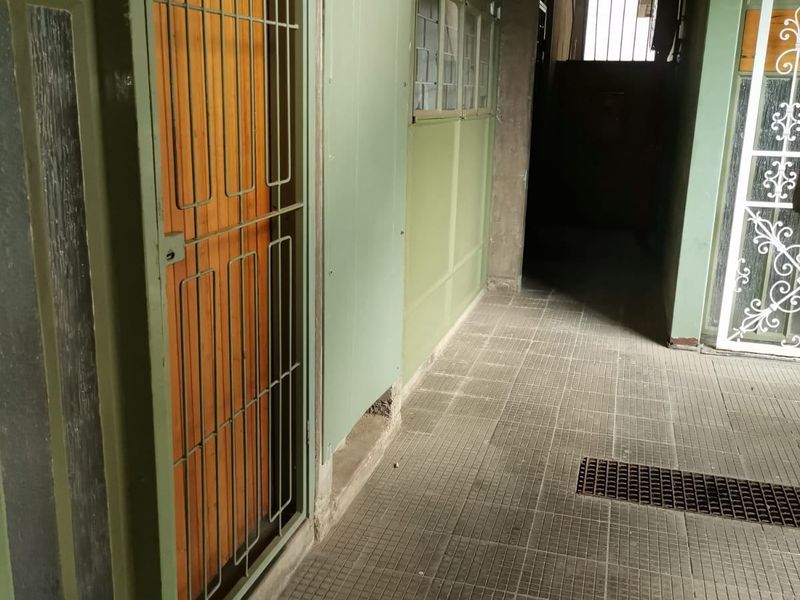 A view of an apartment building corridor featuring tiled flooring, security gates, and dated exterior wall finishes.