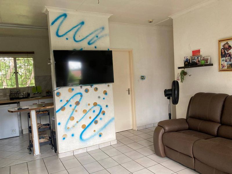 Open plan living and kitchen area featuring tiled flooring and a central structural pillar. The space requires cosmetic updates and wall refinishing.