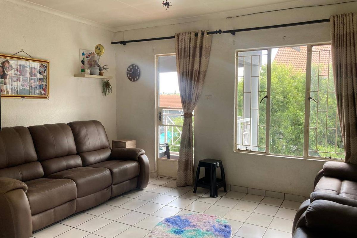A living room featuring tiled flooring, large windows with security bars, and access to an outdoor area through a glass door.