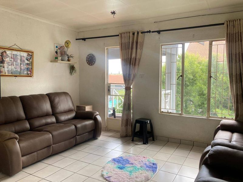 A living room featuring tiled flooring, large windows with security bars, and access to an outdoor area through a glass door.