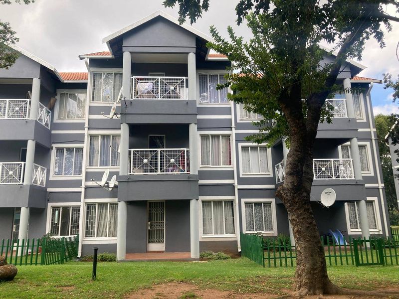 A multi-story apartment building exterior featuring grey facade, white trim, private balconies with metal railings, and a shared garden area.