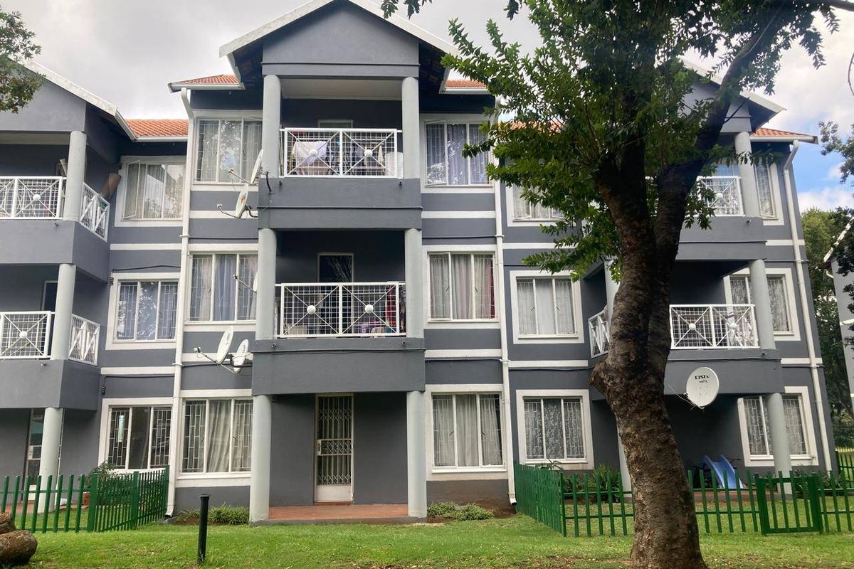 A multi-story apartment building exterior featuring grey facade, white trim, private balconies with metal railings, and a shared garden area.