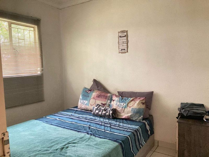 A simple bedroom featuring tiled flooring and a window fitted with venetian blinds.