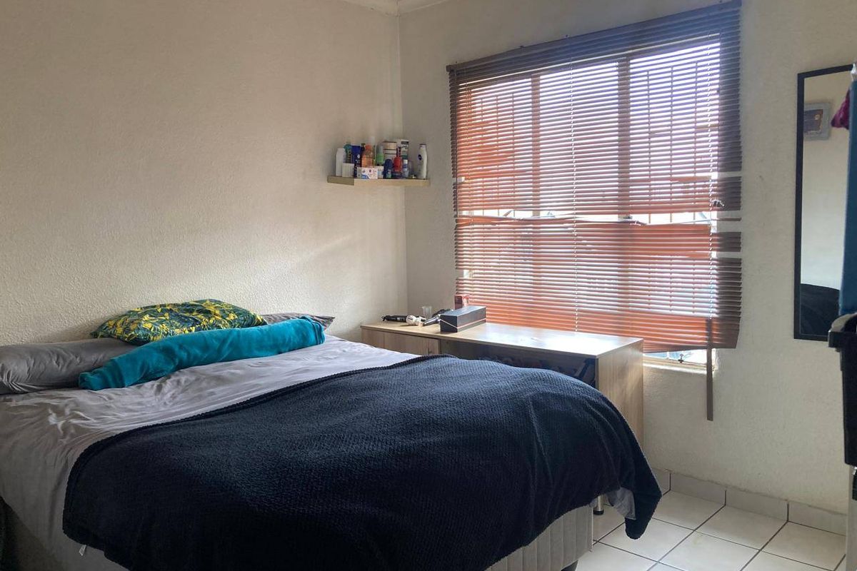 A functional bedroom featuring tiled flooring, a wall-mounted shelf, and venetian blinds providing natural light control.