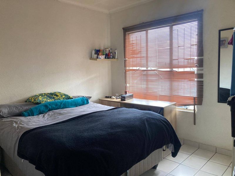 A functional bedroom featuring tiled flooring, a wall-mounted shelf, and venetian blinds providing natural light control.