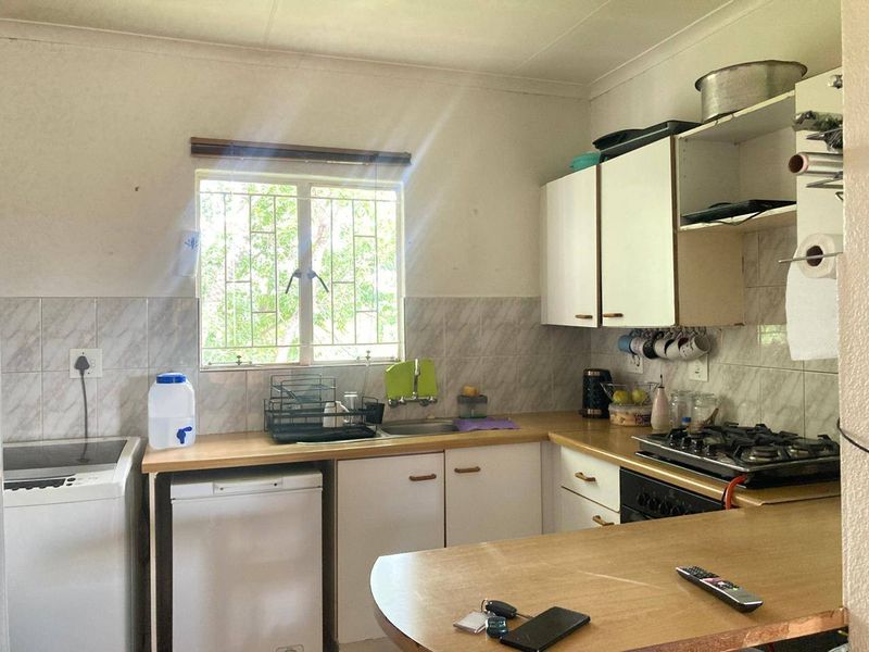 A functional kitchen featuring built-in cabinetry, laminate countertops, a gas hob, and a tiled backsplash, offering potential for modernization.