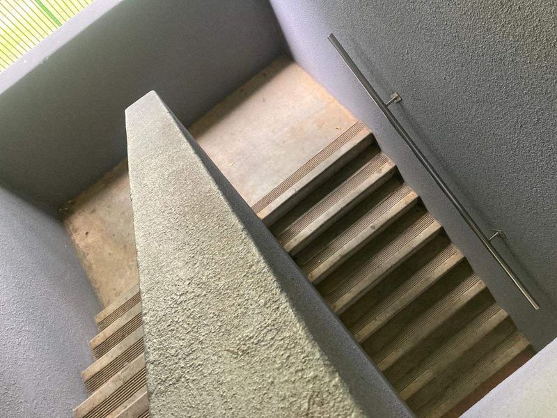 A functional concrete stairwell featuring a metal handrail and textured wall finishes, providing access between levels in the apartment building.